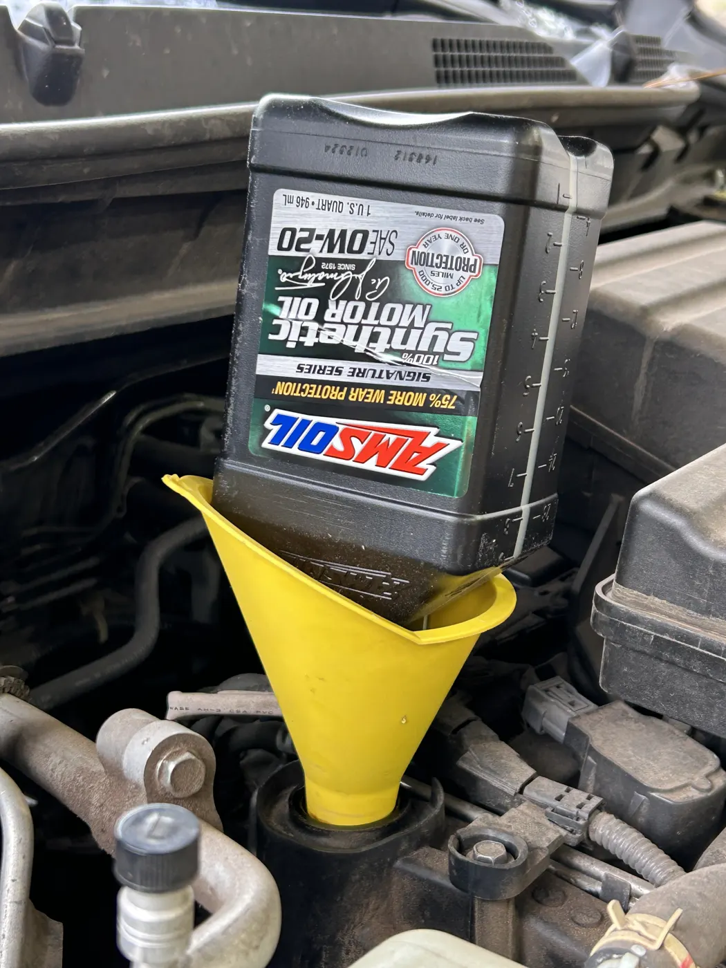 Pouring AMSOIL 0W-40 Signature Series into an engine through a yellow funnel