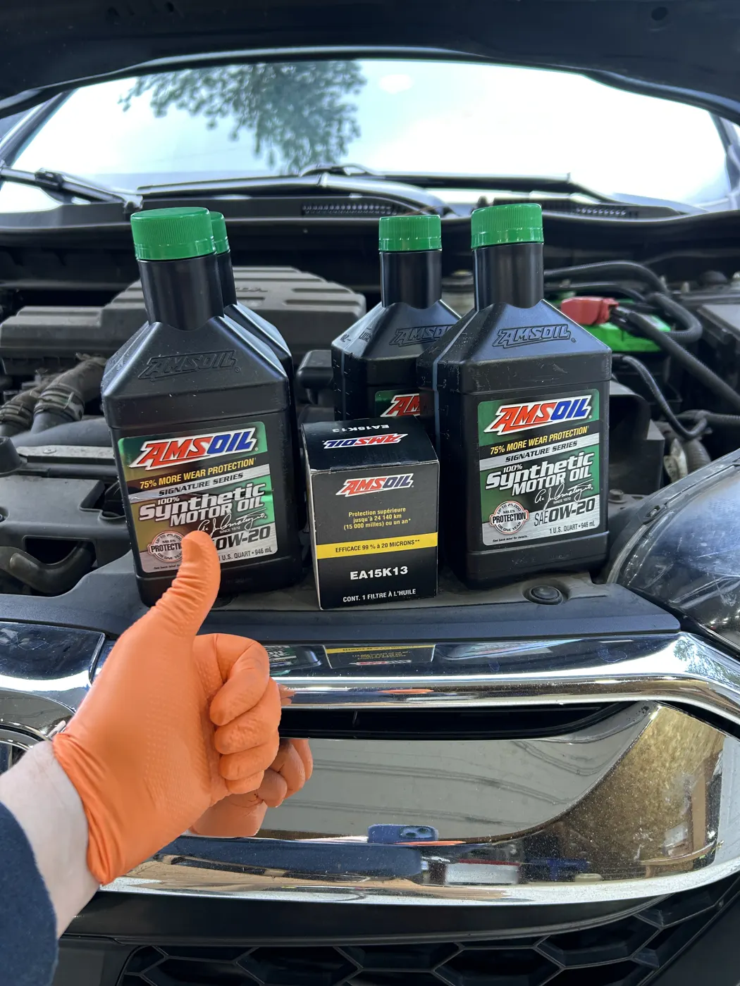 Three bottles of AMSOIL synthetic motor oil on a vehicle bumper